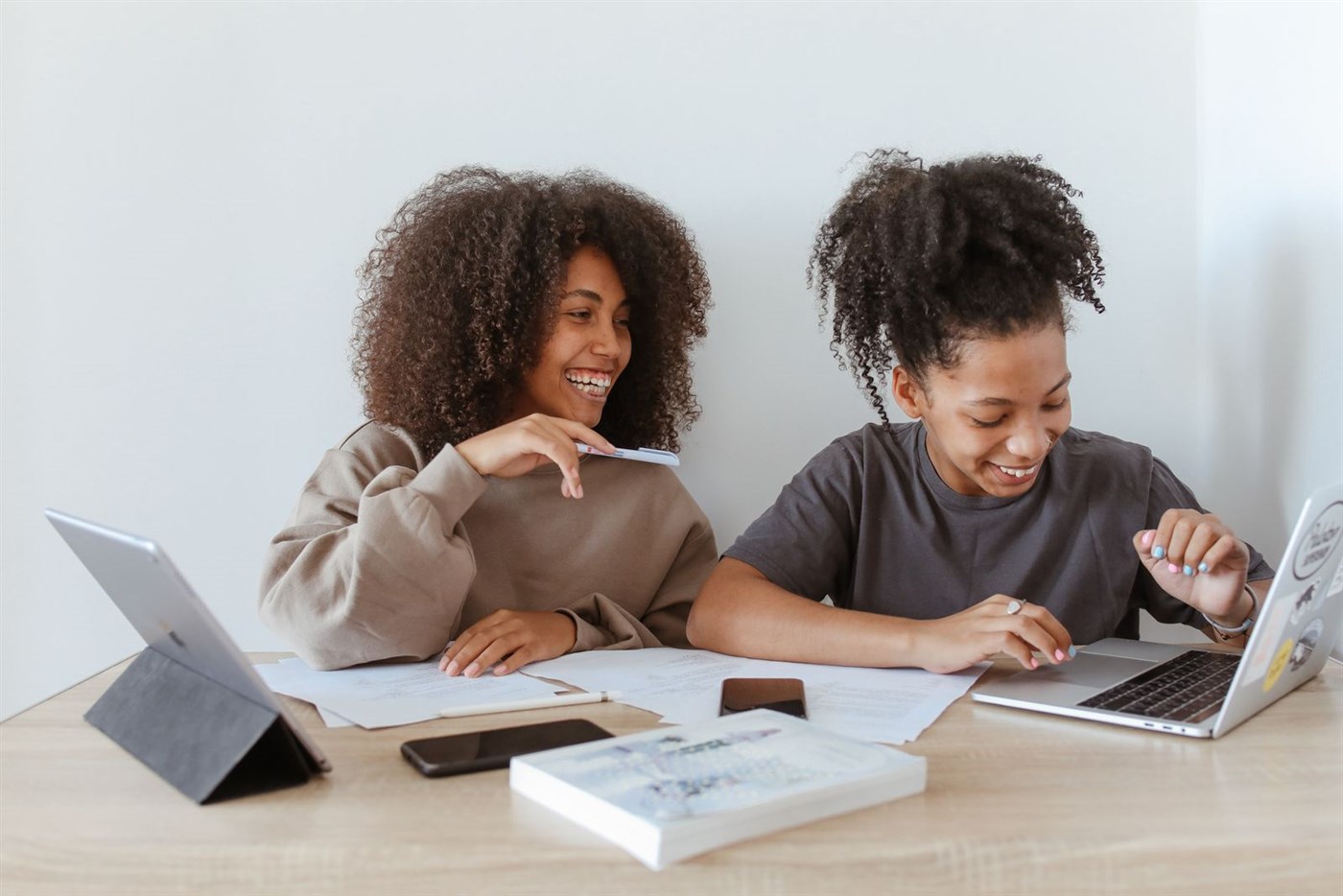 Two students working together at a desk with laptops and papers, laughing